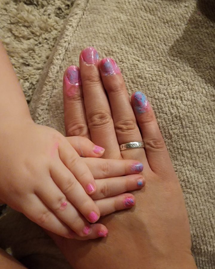 A mother's hand with her little one's hand on top, both with painted nails